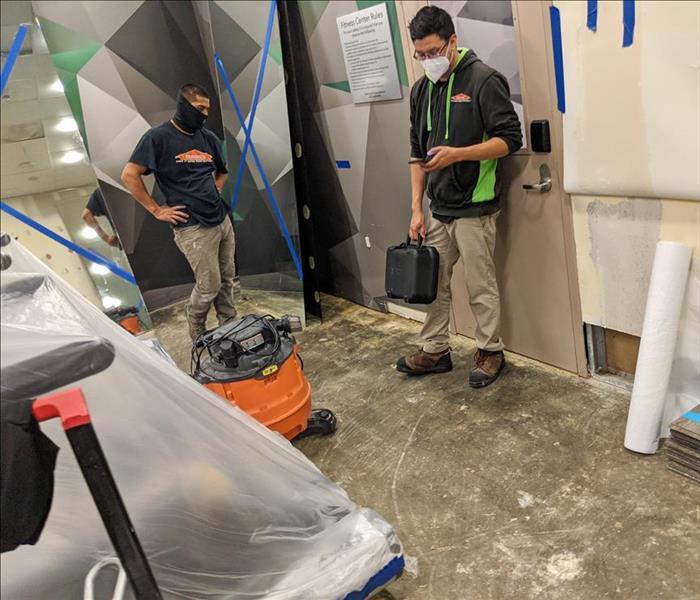 Two SERVPRO technicians setting up water drying equipment in a damaged San Diego business