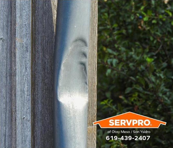 A downspout attached to the side of a home is severely dented.