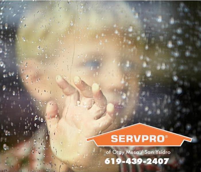 A little boy is looking out of a rain splattered window on a stormy day. 